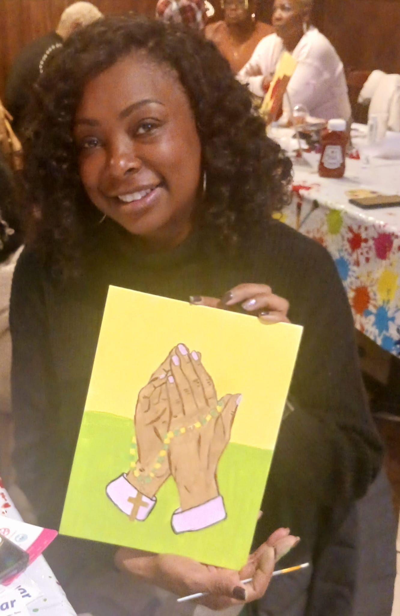 Woman smiling while holding a colorful artwork of praying hands.